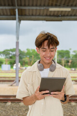 Fototapeta premium Young non binary tourist traveler in train station using tablet computer