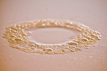 Circle of clear water droplets and condensation forming on smooth flat surface, creating clean and minimal abstract pattern with soft warm tone