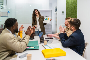 Diverse coworkers clapping hands after a successful presentation held by a young businesswoman in a...