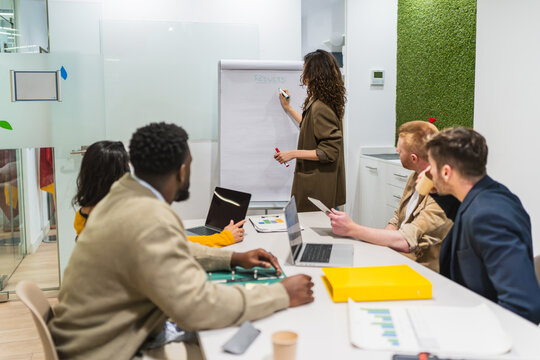 Diverse team collaborating, analyzing data, and strategizing during a presentation in a modern coworking space - Powered by Adobe