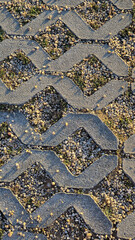A close-up of a patterned pavement with gravel and grass growing through concrete shapes, highlighting texture, geometry, and natural urban integration.