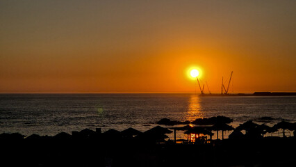 Sunset at Homem do Leme beach in Porto, Portugal, on July 8, 2025, showing silhouetted beach umbrellas and cranes against a golden sky, capturing a peaceful holiday evening by the Atlantic Ocean.