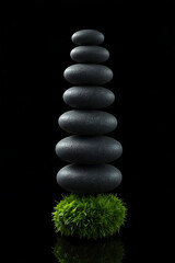 Fototapeta premium The image features a vertical stack of dark gray stones arranged symmetrically against a black background, partially covered in green moss, creating a striking contrast in color and texture.