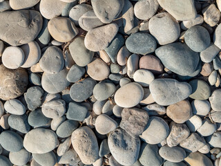 Smooth pebble beach with natural stones and people relaxing by the sea on a sunny day, showing textures of round rocks, hand holding stone and coastal landscape