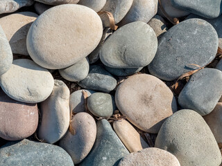 Smooth pebble beach with natural stones and people relaxing by the sea on a sunny day, showing...