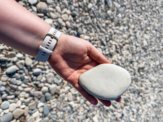Smooth pebble beach with natural stones and people relaxing by the sea on a sunny day, showing textures of round rocks, hand holding stone and coastal landscape