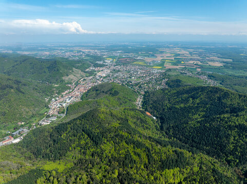 Aerial view of verdant hillsides embrace a quaint town nestled between the forest and the sprawling landscape under a vast sky in Thann, Alsace, France.