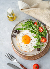 Fried eggs with arugula, ovives  and cherry tomatoes on a plate on a wooden board
