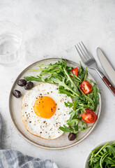 Fried eggs with arugula, ovives  and cherry tomatoes on a plate on a light background