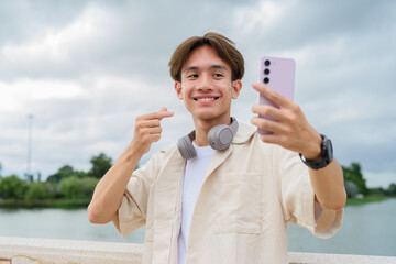 Asian non binary tourist person with headphones relaxing at park near lake using mobile phone
