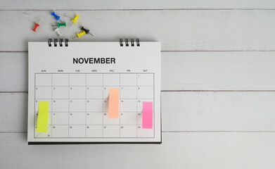 Top view of november appointment calendar with multicolored pins on white tabletop, schedule...