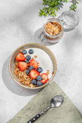 Natural yogurt with granola, blueberry and strawberry in a bowlon a light background