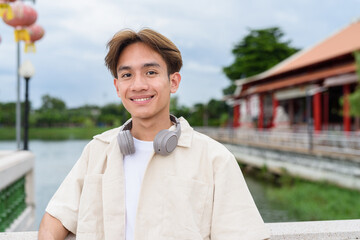 Asian non binary tourist person with headphones relaxing at park near lake