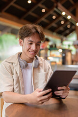 Handsome young non binary man sitting in cafe restaurant using digital tablet computer