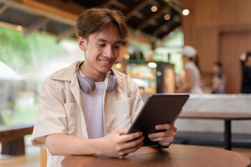 Handsome young non binary man sitting in cafe restaurant using digital tablet computer