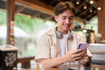 Handsome young non binary man sitting in cafe restaurant using phone