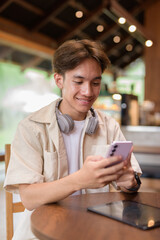 Handsome young non binary man sitting in cafe restaurant using phone