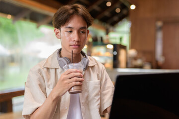 Handsome young non binary man sitting in cafe restaurant using laptop computer