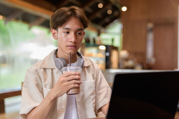 Handsome young non binary man sitting in cafe restaurant using laptop computer