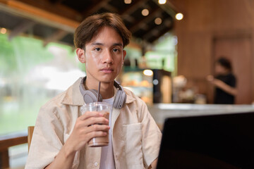 Handsome young non binary man sitting in cafe restaurant using laptop computer