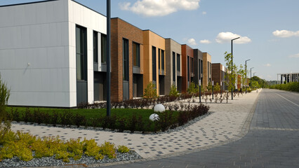Modern residential street with row of stylish townhouses with varied architectural facades and manicured landscaping. Contemporary design new urban development and comfortable living spaces. 