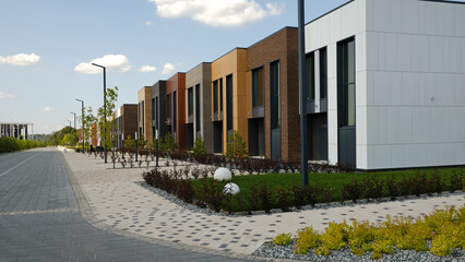 Modern residential street with row of stylish townhouses with varied architectural facades and manicured landscaping. Contemporary design new urban development and comfortable living spaces. 
