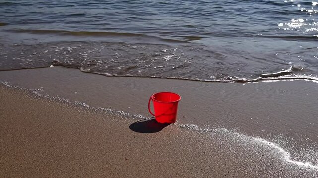 Red plastic cup sitting on sandy shore, waves lapping, bright sunlight illuminating tranquil beachscape