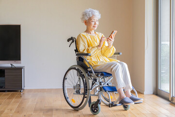 車椅子に乗ってスマホを使うシニア女性