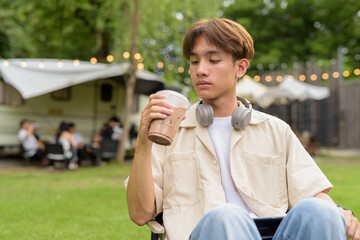 Young non binary person having road trip and camping with friends drinking chocolate drink