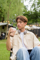 Young non binary person having road trip and camping with friends drinking chocolate drink