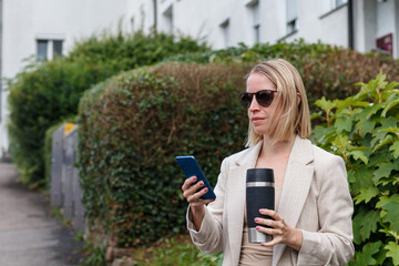 Businesswoman holding coffee and using smartphone


