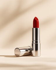 Vibrant red lipstick stands elegantly on pale cream seamless background, showcasing its sleek silver packaging. soft lighting enhances its glossy finish, creating captivating allure