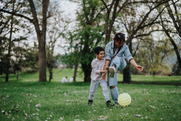 An Asian mother and her cheerful child playing joyfully with a ball in a park. Green grass,...