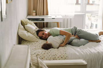 Home portrait of a baby boy with mother on the bed relaxing and playing in the bed at the weekend together, lazy morning, warm and cozy scene. Mom holding and kissing her child. Mother day concept