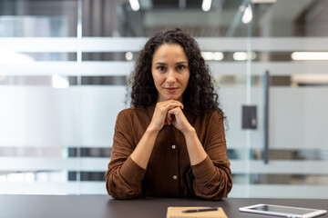 A businesswoman looks directly at the camera, her hands clasped thoughtfully in front of her, a...