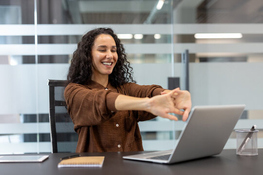 Fototapeta A smiling woman stretches at her desk, taking a break from work. Office workspace.