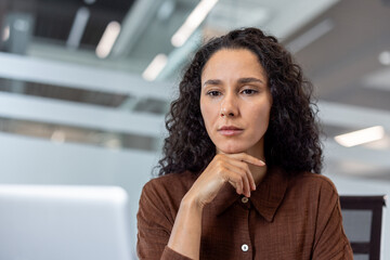 A thoughtful businesswoman with curly hair considers a decision, resting her chin on her hand in a...