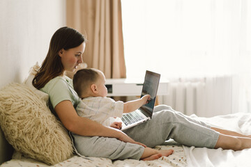 Portrait of happy young mother with little baby using laptop at home. Together, smiling mom...