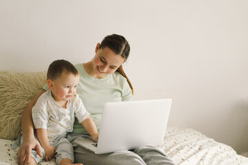 Portrait of happy young mother with little baby using laptop at home. Together, smiling mom...