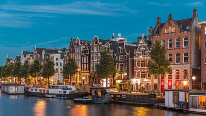 Panoramic timelapse hyperlapse of the illuminated famous Dancing Houses along the Amstel River day to night transition. Amsterdam, Netherlands