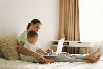 Portrait of happy young mother with little baby using laptop at home. Together, smiling mom...