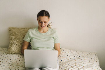 Young beautiful woman working on laptop on bed. Concepts of technology and freelance work.