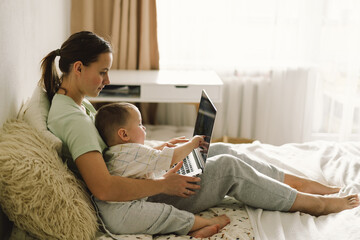 Portrait of happy young mother with little baby using laptop at home. Together, smiling mom...