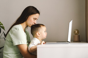 Portrait of happy young mother with little baby using laptop at home. Together, smiling mom...