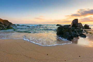 landscape by the sea at sunrise in summer. beautiful beach with rocks washed by calm waves in...