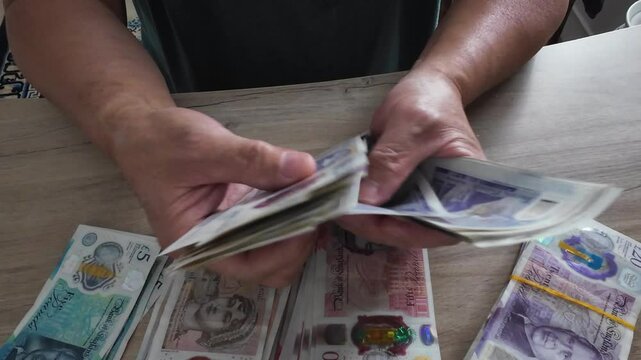 A person counting Pound Sterling bank notes on a desk.