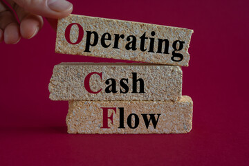 Concept words OCF-operating cash flow on brick blocks. Beautiful red background. Businessman hand....