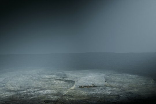 A low-angle shot depicts a dimly lit, misty stone platform, possibly outdoors, with a subtle light source illuminating the scene from above, creating a mysterious and atmospheric mood.