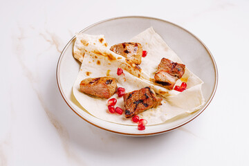 Grilled meat served on flatbread with pomegranate seeds in a white bowl