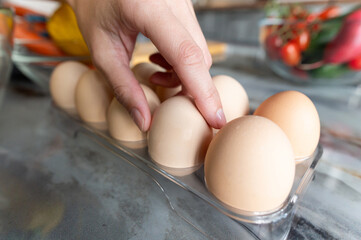 Close-up of woman's hand taking chicken egg from tray with fingers. Food preparation concept,...